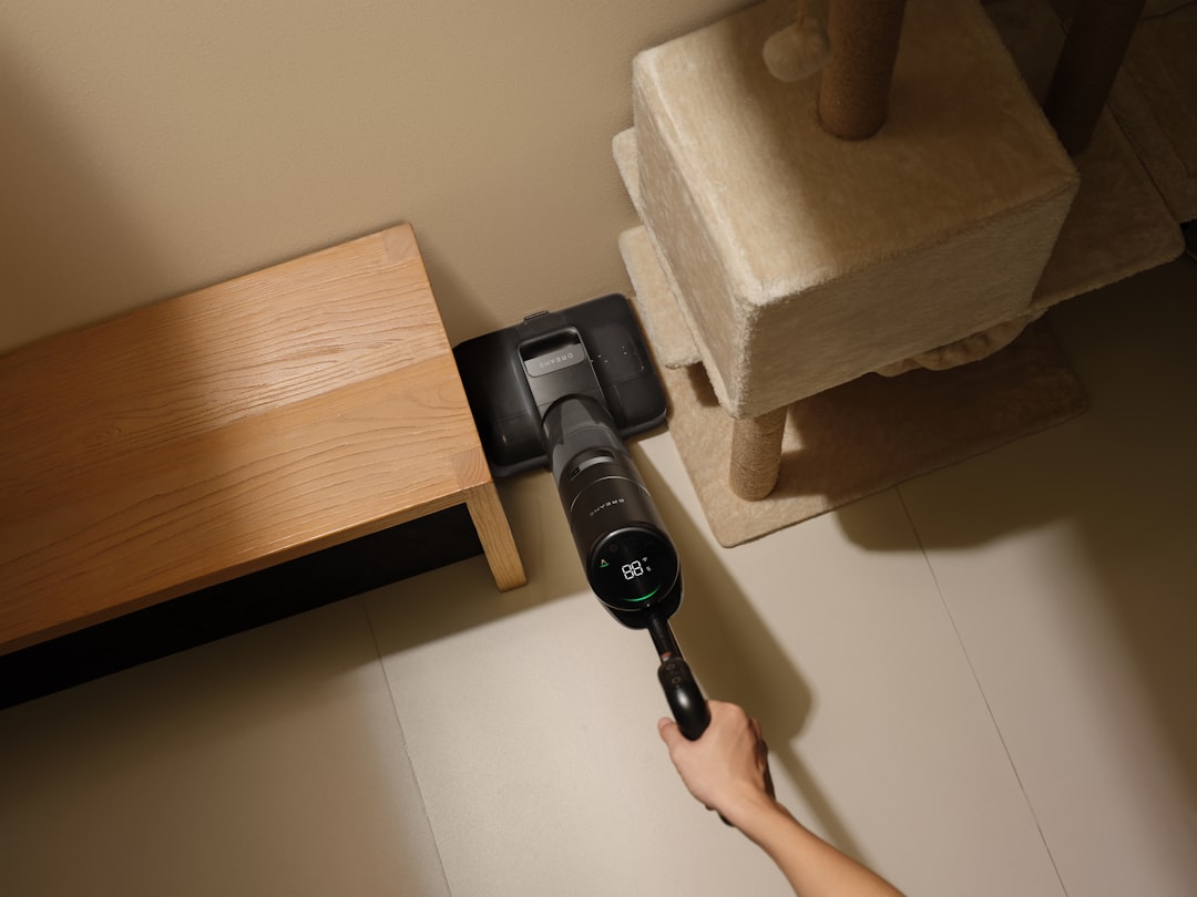 Person vacuuming a corner with a cordless vacuum.