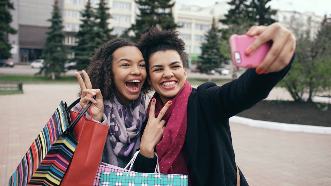 Two smiling women taking a selfie with shopping bags.